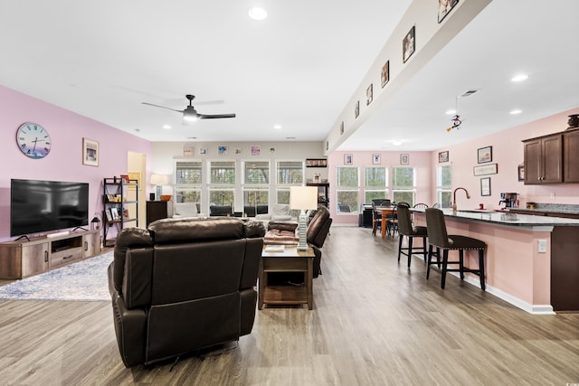 living room featuring light wood-type flooring, ceiling fan, and sink