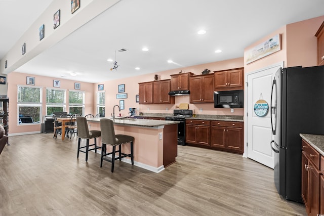 kitchen featuring a breakfast bar, light wood-type flooring, a center island with sink, and black appliances