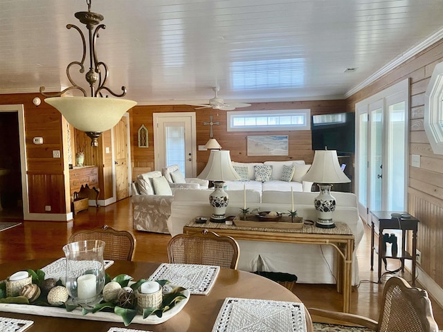 living room featuring wood-type flooring, crown molding, wooden walls, and ceiling fan