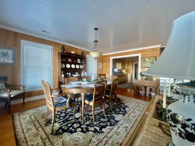 dining area featuring wooden walls, wood finished floors, visible vents, and ornamental molding