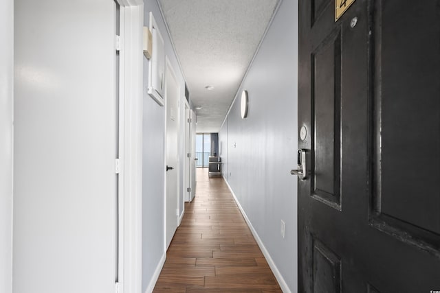 hall featuring dark wood-style floors, a textured ceiling, and baseboards