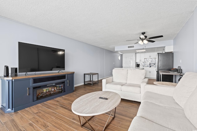 living area with a textured ceiling, wood finished floors, visible vents, and a ceiling fan