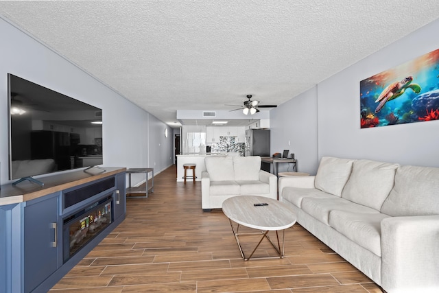 living room featuring dark wood-style floors, ceiling fan, visible vents, and a textured ceiling