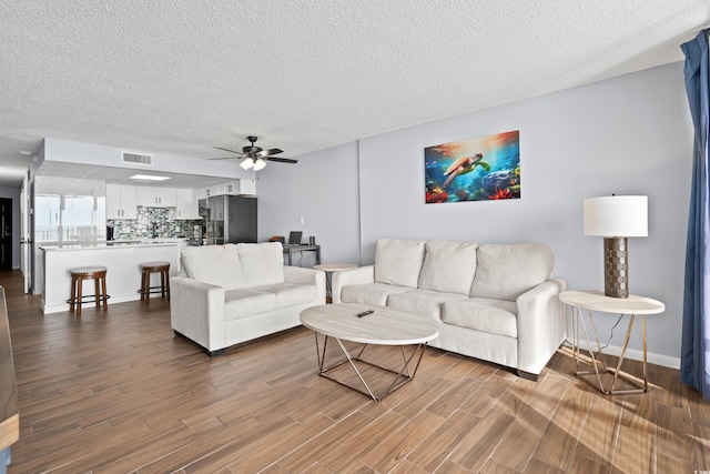 living room with dark wood-style flooring, visible vents, ceiling fan, and a textured ceiling