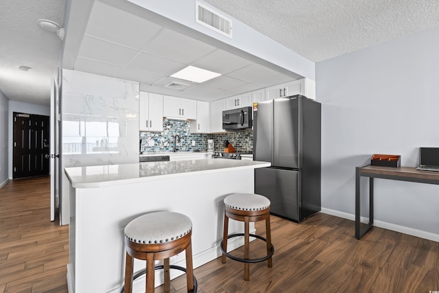 kitchen with tasteful backsplash, visible vents, freestanding refrigerator, white cabinetry, and black microwave