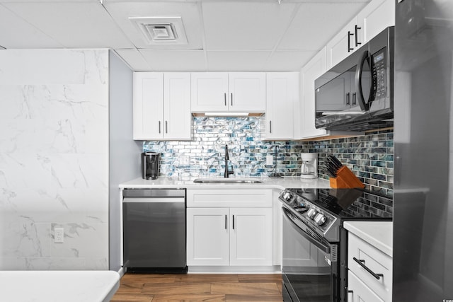 kitchen featuring stainless steel appliances, wood finished floors, a sink, white cabinets, and light countertops