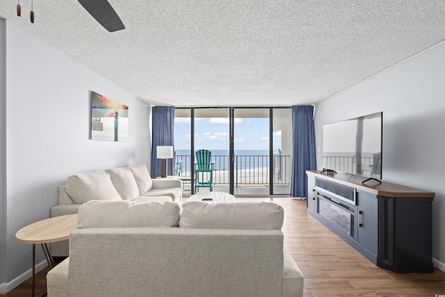 living room featuring a wall of windows, light wood-type flooring, a textured ceiling, and baseboards