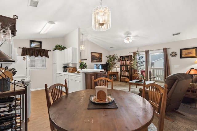 dining space featuring ceiling fan with notable chandelier, lofted ceiling, and light wood-type flooring