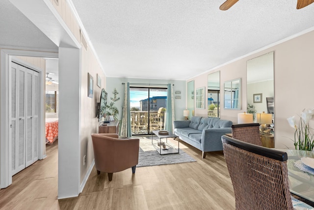 living room featuring ceiling fan, light hardwood / wood-style floors, ornamental molding, and a textured ceiling