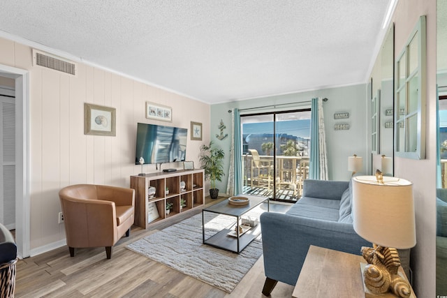 living room featuring a textured ceiling, light hardwood / wood-style floors, and crown molding