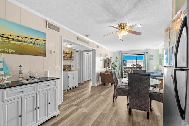 dining room featuring ceiling fan, crown molding, wood walls, light hardwood / wood-style floors, and a textured ceiling