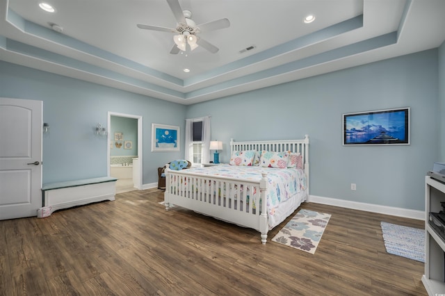 bedroom with a raised ceiling, connected bathroom, ceiling fan, and dark hardwood / wood-style flooring