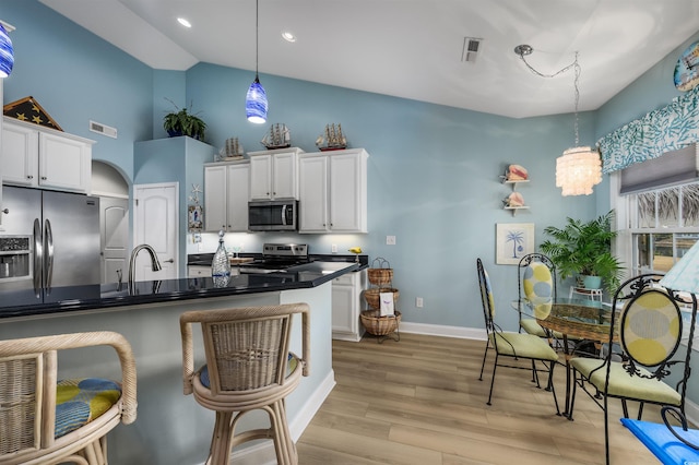 kitchen with stainless steel appliances, an inviting chandelier, white cabinets, light hardwood / wood-style floors, and hanging light fixtures