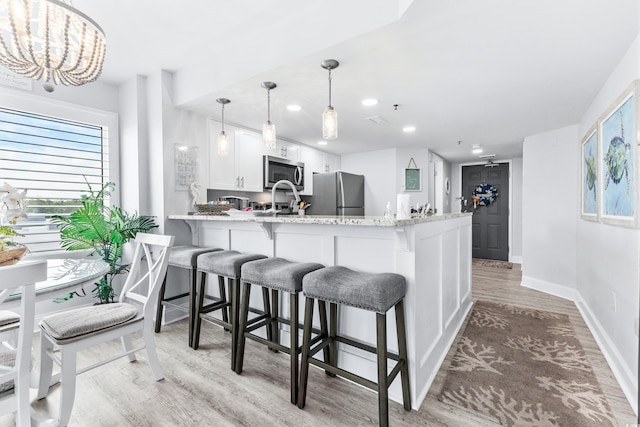 kitchen featuring white cabinets, hanging light fixtures, light hardwood / wood-style flooring, appliances with stainless steel finishes, and kitchen peninsula