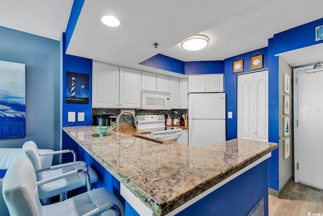 kitchen featuring white appliances, backsplash, a kitchen breakfast bar, white cabinets, and light wood-type flooring