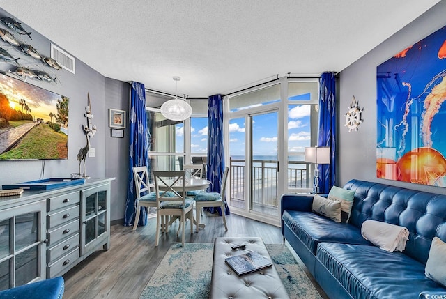 living room with a water view, a wall of windows, wood-type flooring, and a textured ceiling