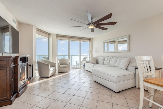 living room with ceiling fan, light tile patterned floors, expansive windows, a textured ceiling, and a water view