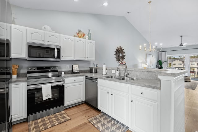 kitchen featuring lofted ceiling, kitchen peninsula, sink, appliances with stainless steel finishes, and white cabinetry