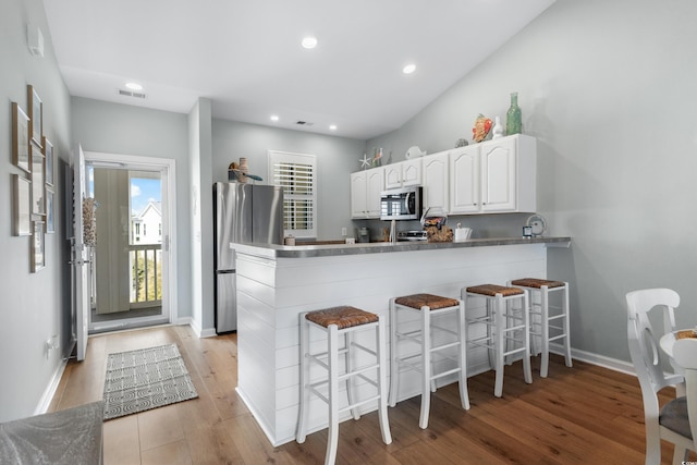 kitchen with kitchen peninsula, light hardwood / wood-style floors, a kitchen bar, white cabinets, and appliances with stainless steel finishes