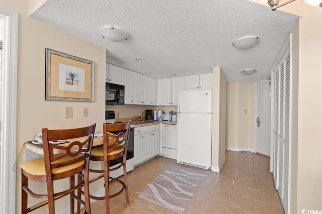 kitchen featuring white appliances, a textured ceiling, a sink, white cabinetry, and light tile patterned flooring