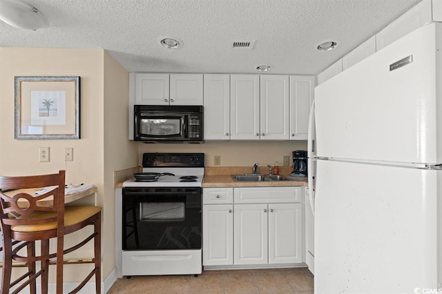 kitchen featuring black microwave, freestanding refrigerator, electric range, a sink, and white cabinets