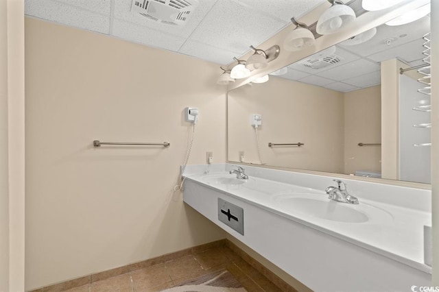 bathroom with a paneled ceiling, tile patterned flooring, baseboards, and double vanity