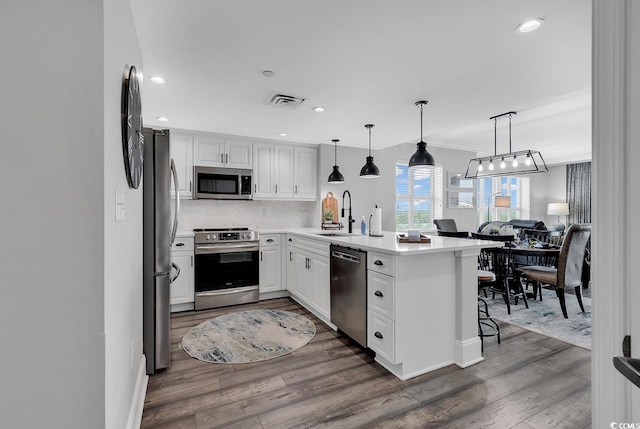 kitchen featuring kitchen peninsula, appliances with stainless steel finishes, pendant lighting, white cabinets, and a breakfast bar area