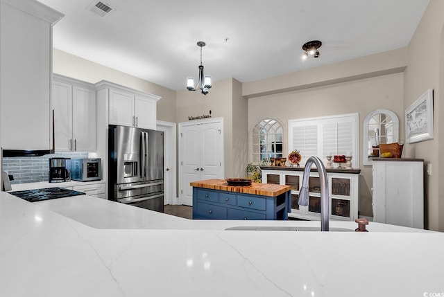 kitchen with a center island, stainless steel refrigerator with ice dispenser, butcher block countertops, pendant lighting, and white cabinets