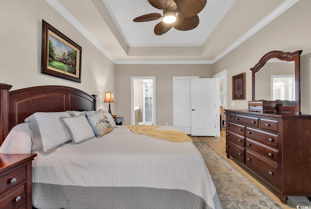 bedroom with ensuite bathroom, ceiling fan, light wood-type flooring, and a tray ceiling