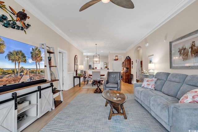 living room with crown molding, ceiling fan with notable chandelier, and light wood-type flooring