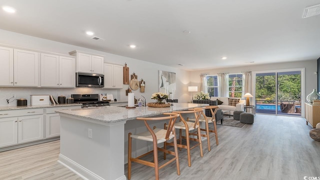 kitchen with stove, a kitchen breakfast bar, white cabinets, light hardwood / wood-style floors, and an island with sink