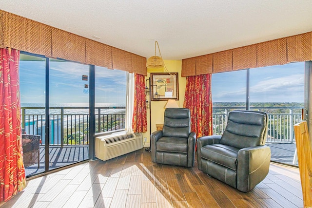 living area featuring a water view, plenty of natural light, a wall mounted AC, and hardwood / wood-style floors