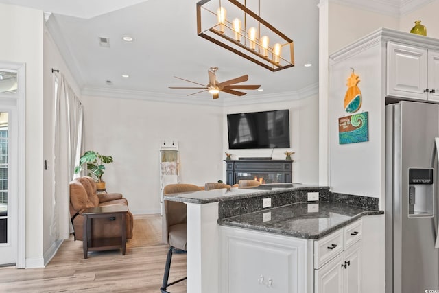 kitchen featuring white cabinets, stainless steel refrigerator with ice dispenser, a kitchen bar, and ornamental molding