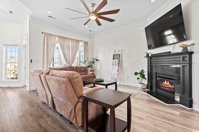 living room featuring ceiling fan, crown molding, light wood-type flooring, and a fireplace