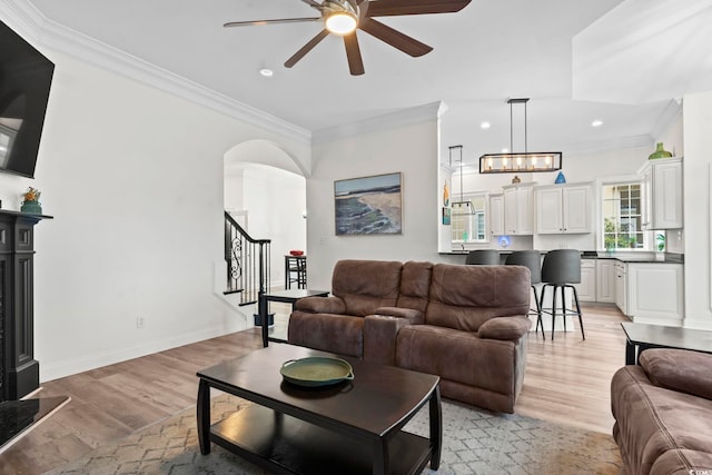 living room with ceiling fan with notable chandelier, light hardwood / wood-style floors, and ornamental molding