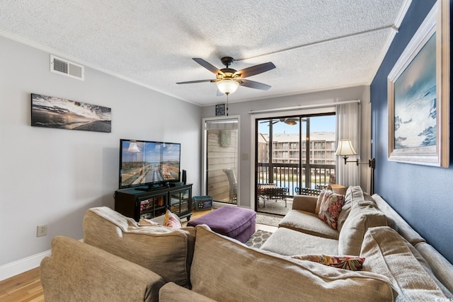 living area with wood finished floors, visible vents, baseboards, a ceiling fan, and ornamental molding