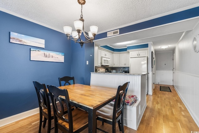 dining space with a textured ceiling, light wood-style flooring, visible vents, and crown molding