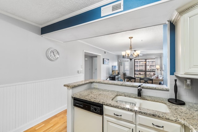 kitchen featuring white dishwasher, a wainscoted wall, a sink, visible vents, and light wood finished floors