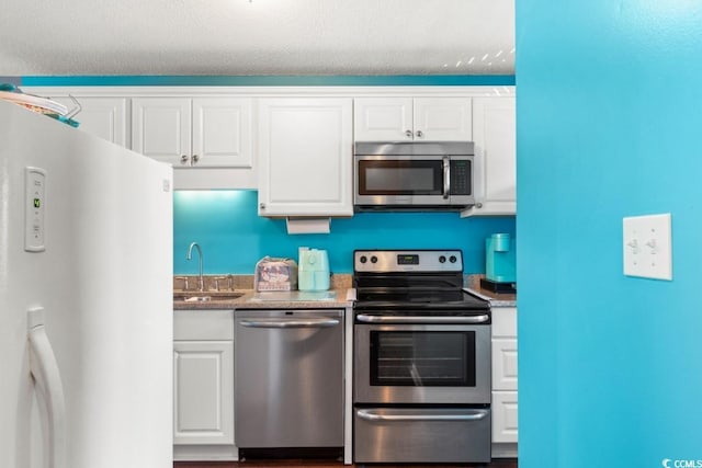 kitchen with white cabinetry, appliances with stainless steel finishes, dark stone counters, and a sink