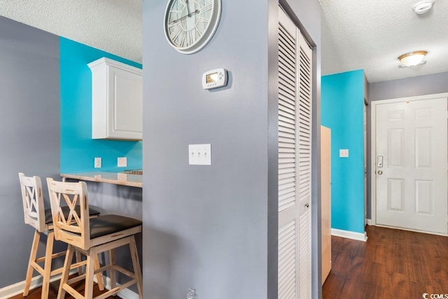 interior space with light stone counters, dark wood-type flooring, white cabinets, a textured ceiling, and baseboards