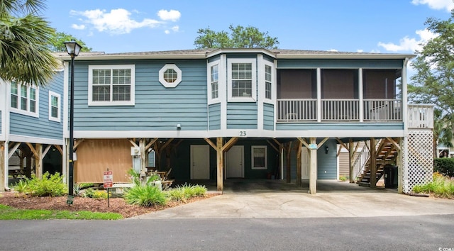 coastal inspired home with stairs, a carport, concrete driveway, and a sunroom