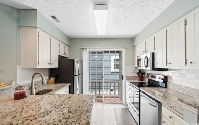 kitchen featuring light wood finished floors, tasteful backsplash, visible vents, stainless steel appliances, and a sink