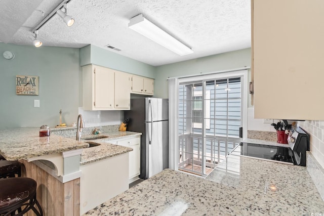 kitchen featuring a peninsula, a sink, visible vents, freestanding refrigerator, and light stone countertops