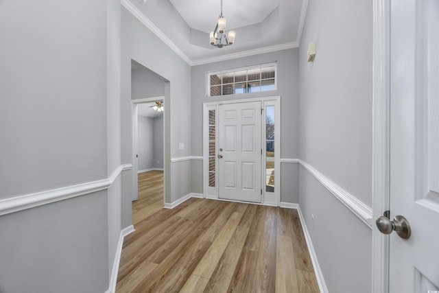 entryway featuring ceiling fan with notable chandelier, a tray ceiling, crown molding, and light hardwood / wood-style floors