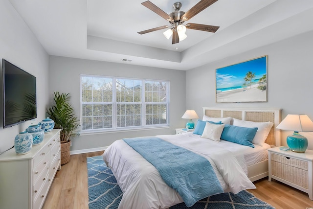 bedroom featuring a tray ceiling, ceiling fan, and light wood-type flooring