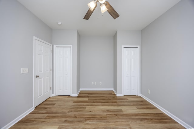 unfurnished bedroom featuring ceiling fan, light hardwood / wood-style flooring, and two closets