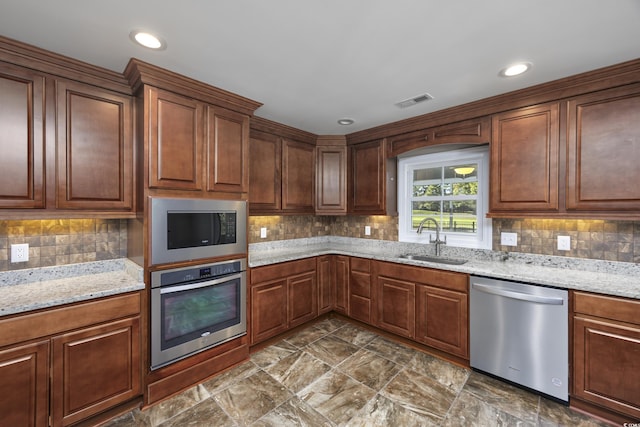 kitchen featuring tasteful backsplash, light stone counters, sink, and appliances with stainless steel finishes