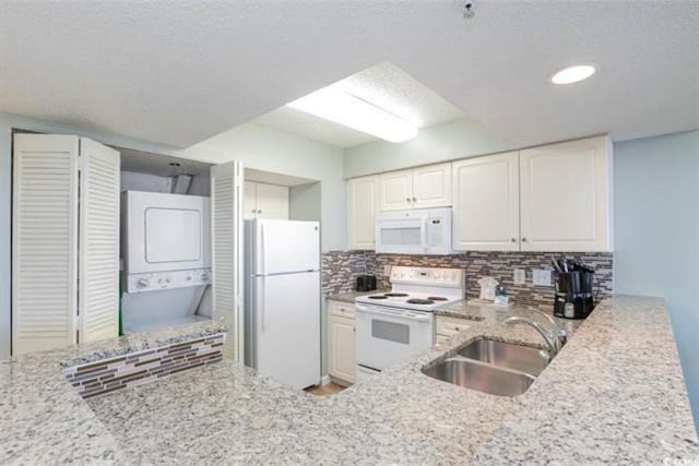 kitchen with backsplash, white appliances, sink, stacked washer and dryer, and white cabinetry