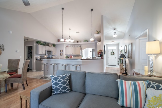 living room featuring high vaulted ceiling, light hardwood / wood-style floors, and an inviting chandelier