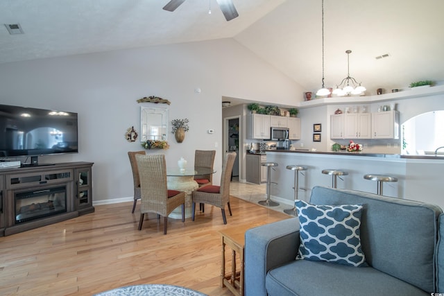 interior space featuring ceiling fan with notable chandelier, high vaulted ceiling, and light hardwood / wood-style flooring